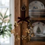 Gold floral Christmas wreath with clear bead accents and burgundy bow hanging on a rustic wooden cabinet