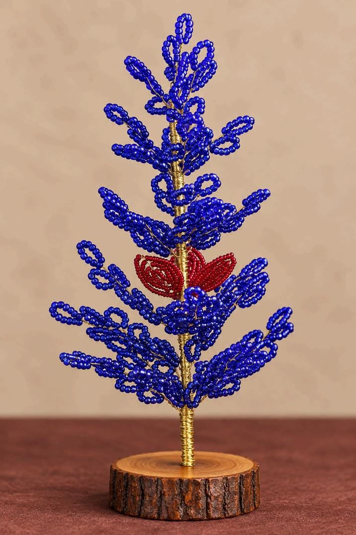 Blue beaded Christmas tree with red floral accent, gold-tone stem and rustic wooden base